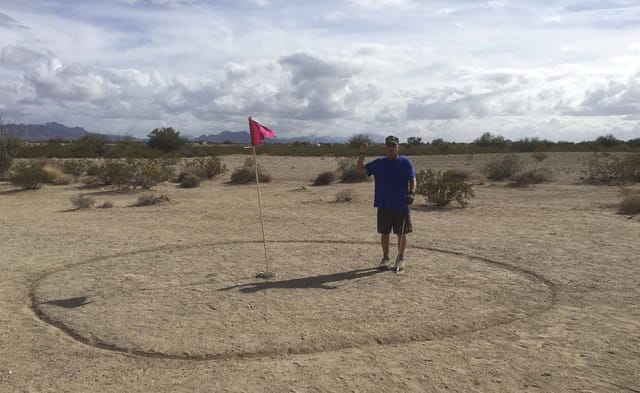 Desert golf: a golfer beside the flag on a dirt green